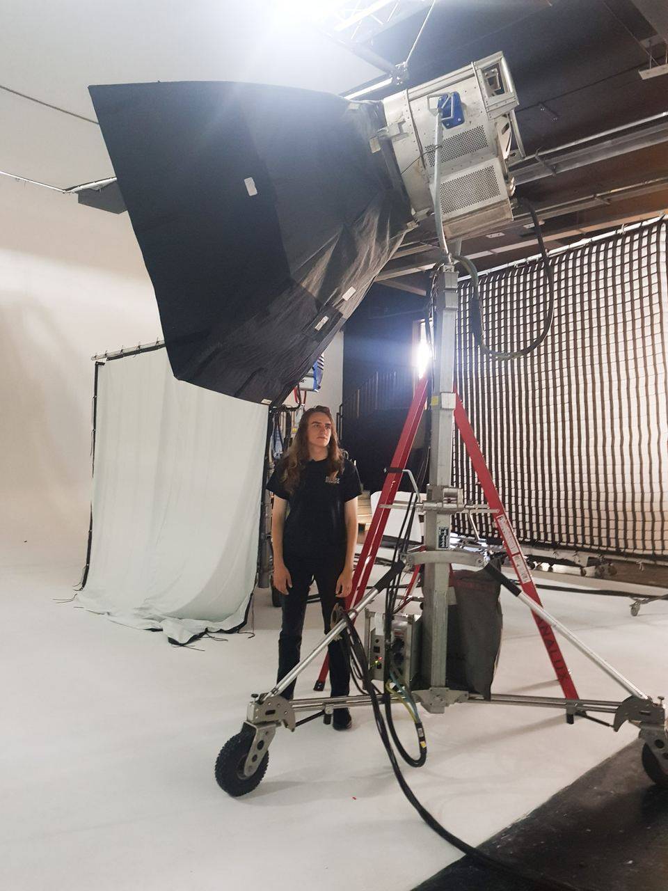 Joël Hainzl with long hair standing in a white cyclorama studio at Big Sky Studios in London beneath a large softbox and an HMI lamp on a stand, 2019