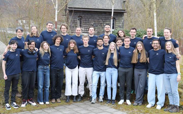 CDTM Class of Spring 2025 group photo, around thirty students in navy CDTM shirts in front of a wooden chapel