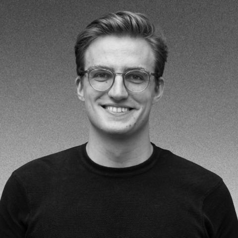 Joël Hainzl, black and white headshot, smiling in round glasses and a dark crew neck