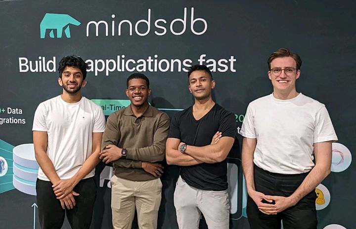 Joël Hainzl, right, with three fellow winners in front of the MindsDB stage wall at the MindsDB hackathon in San Francisco