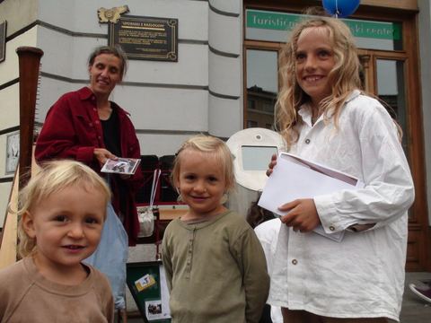 A mother holding a CD and three blond children in front of a tourist information center, a harp at the left edge