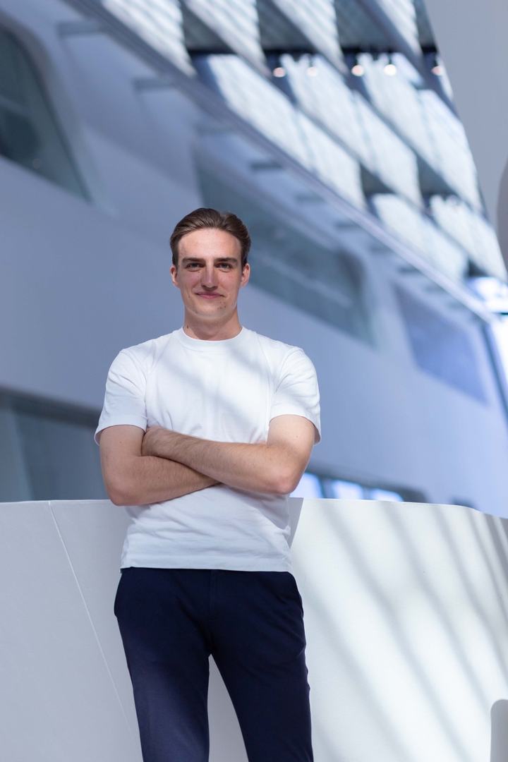 Joël Hainzl with arms crossed in a white t shirt in the atrium of the WU Vienna Library and Learning Center